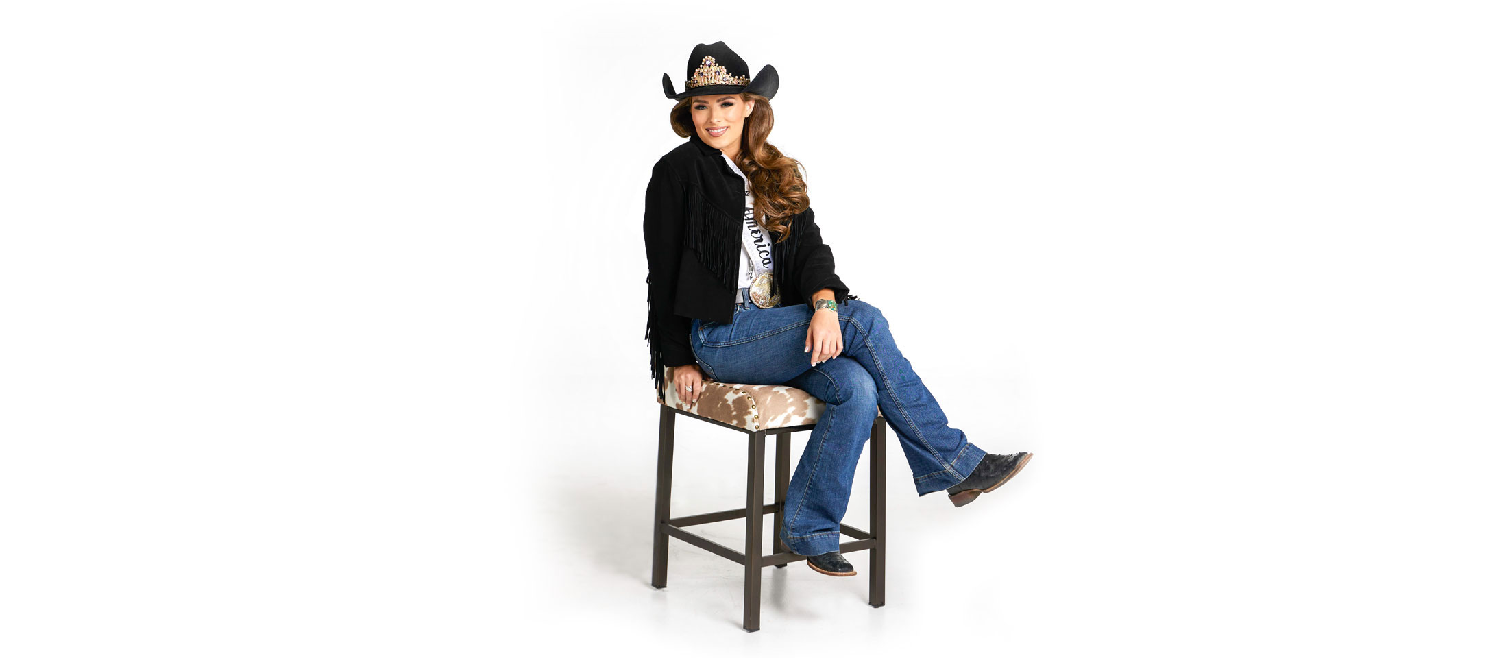 Miss Rodeo America sentada en una silla con las piernas cruzadas sonriendo a la cámara